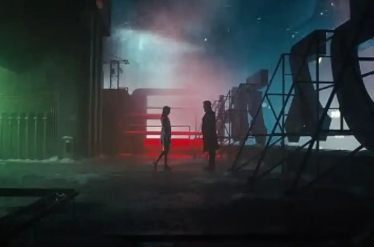 Un homme et une femme androïde face à face la nuit sur un toit, avec des lumières colorées en arrière-plan
